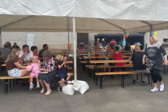 Lidé pod přístřeškem na lavičkách.