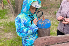 Chlapec venku lupou zkoumá přírodu.