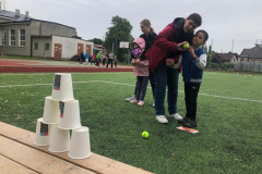 Chlapec s paní asistentkou hází míčky na pyramidu z kelímků.