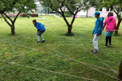 Žáci prolézají pavučinu zavěšenou mezi stromy.