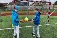 Žáci balancují s míčkem na plastových tyčkách.