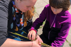 Dívka s paní učitelkou plete velikonoční pomlázku.