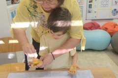 Chlapec ve žluté obtiskává ruku s paní asistentkou.