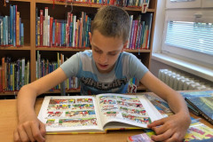 Chlapec si v knihovně prohlíží  knihu.