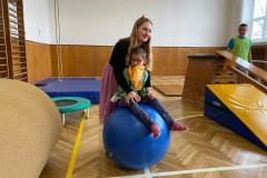 Paní učitelka s dívkou na gymballu v tělocvičně.
