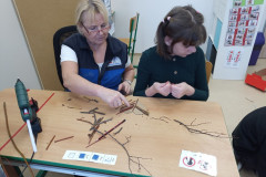 Dívka s paní asistentkou skládá větvičky na karton.