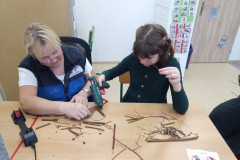 Dívka s paní asistentkou skládá větvičky na karton.