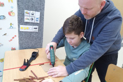 Chlapec s panem asistentem lepí větvičku na karton.