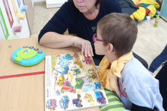 Dívka si čte s paní asistentkou v obrázkové knížce.