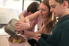 Žáci s paní učitelkou cedí přes cedník.