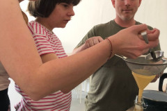 Žáci s paní učitelkou cedí přes cedník a slévají do lahviček.