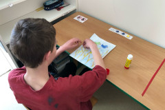 Chlapec ve výtvarce lepí ptáčky na výkres.