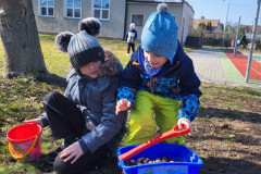 Žáci si hrají na školním hřišti s dětským vozíčkem a přírodninami.