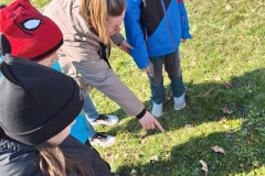 Žáci s paní asistentkou zkoumají přírodu na školní zahradě.