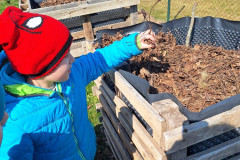 Chlapec dává staré listí do vyvýšeného záhonu.