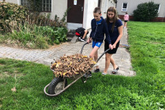 Chlapec s paní asistentkou odváží listí.