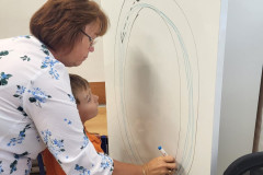 Chlapec s paní asistentkou procvičují grafomotoriku u tabule.