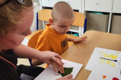 Chlapec s paní vychovatelkou obtiskává lístek na papír.