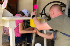 Pan asistent s dívkou dojí dřevěnou kozu.